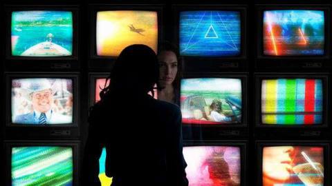 Diana Prince (Gal Gadot) looking at a wall of 12 TVs in Wonder Woman 1984