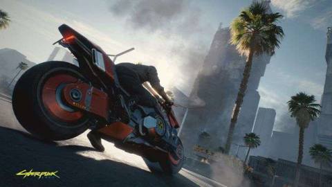 The main character, Vi, in Cyberpunk 2077 sits atop a nuclear-powered red motorcycle in Night City. In the background the city burns.