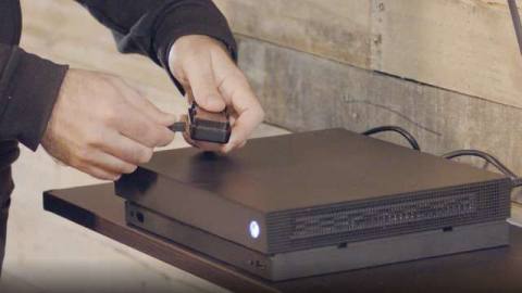 two hands hold a small dongle over an Xbox One X console