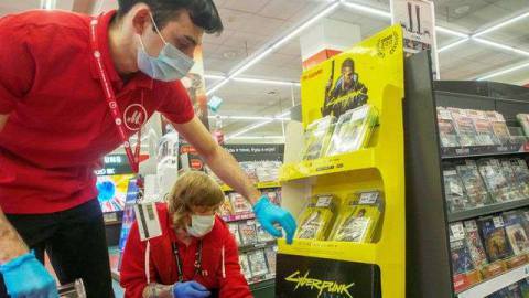 store employees wearing face masks and gloves adjust a Cyberpunk 2077 display