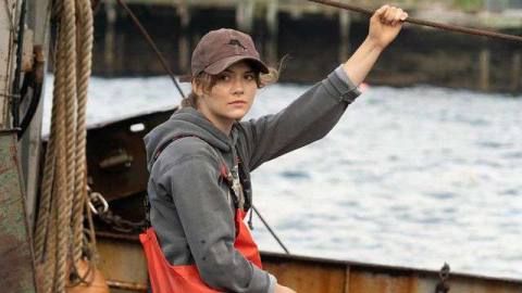 Emilia Jones as Ruby in CODA hanging on to a boat rope and wearing a sweatshirt and orange fisherman pants