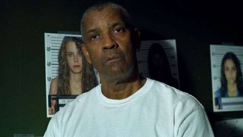 Denzel Washington wears a white t-shirt and stands in front of a green wall with pictures of murdered women in The Little Things