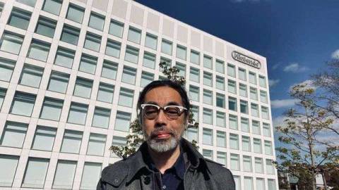 a man with glasses standing in front of Nintendo’s blocky shaped headquarters building 