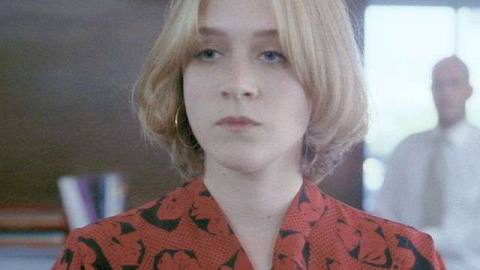 Chloë Sevigny stands in close up in a red blouse as her boss lurks behind her out of focus in Demonlover