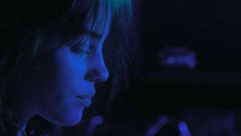 Billie Eilish in profile onstage in blue light.