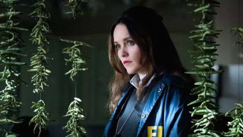 Clarice Starling stands in a dark room surrounded by dangling strings of green vegetables in Clarice