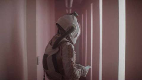 A space-suited “knocker” in a long pink hallway full of bright white lights in the science fiction movie Doors