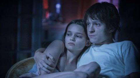 Cherry (Tom Holland) and his wife Emily (Ciara Bravo), bathed in blue light, sit strung out on the couch after shooting up heroin