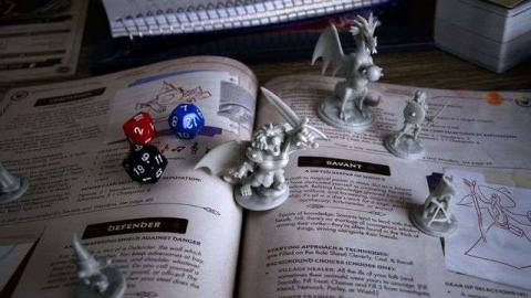 Dice and miniatures, including a plastic Manticore, stand on top of the Quest of Yore rulebook with a few dice. 