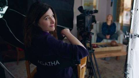 Agatha Harkness smirks over her shoulder as she sits in a director’s chair in WandaVision, probably celebrating that she didn’t get killed off like most MCU villain