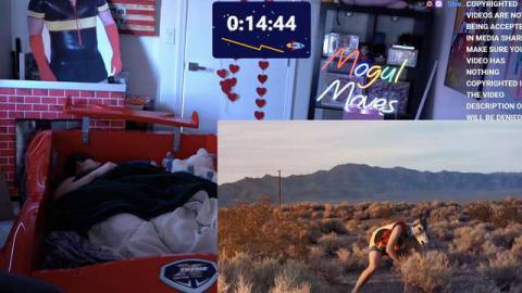 An adult man sleeping in a red racer bed. There’s an overlay of a video, which shows a person wearing a giraffe mask digging in the dirt.