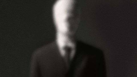 A blurry picture of a faceless man in a black suit and tie, the Slenderman