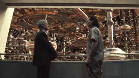 Loki and Agent Mobius stand in front of a brutalist window looking at the massive city/structure of the Time Variance Authority in Loki. 