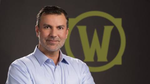 A press photo of former World of Warcraft creative director Alex Afrasiabi in front of the game’s logo.
