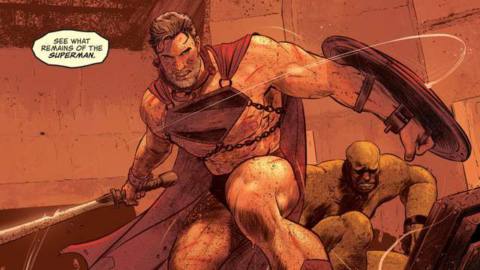 A grey-haired and bloodied Superman springs out of a gladiator cage on War World, dressed only in his cape, underwear, boots, and a Superman symbol chained to his chest. He brandishes a sword and shield as the announcer cries “See what remains of the Superman,” in Future State: Superman Worlds of War #1, DC Comics (2021).