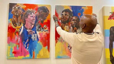 a photo of artist Charly Palmer putting up a painting of Kareem Abdul-Jabbar, Kevin Durant, and Dirk Nowitzki next to a similar painting