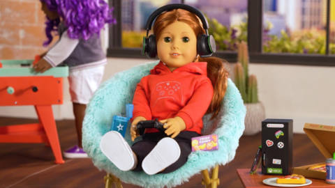 an american girl doll in a cool chair holding a controller