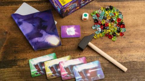 A small wooden hammer, with cards, dice, and plastic gems sitting on a table.