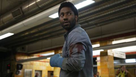 Tenet’s John David Washington, bandaged and bloody, looks over his shoulder cautiously in Netflix’s Beckett