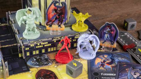 A collection of Gargoyles miniatures with assorted custom stone-colored dice, cards, and a 3D building that rises off the table.