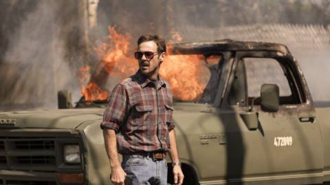 A man stands in front of a truck that’s on fire in Narcos: Mexico season 3 