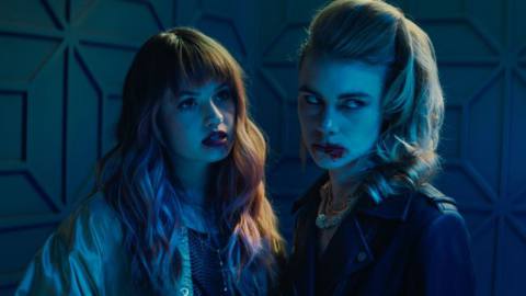 Two of Night Teeth’s vampires, Blaire (Debby Ryan) and Zoe (Lucy Fry), stand together in a dimly lit room, with their mouths bloody