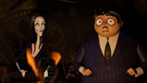 Morticia and Gomez Addams in the dark, staring wide-eyed at something offscreen
