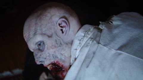 A research scientist turned zombie turns toward the camera in a still from Resident Evil: Welcome to Raccoon City