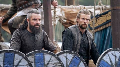 Canute and Harald stand behind their shields on a battlefield in Vikings: Valhalla
