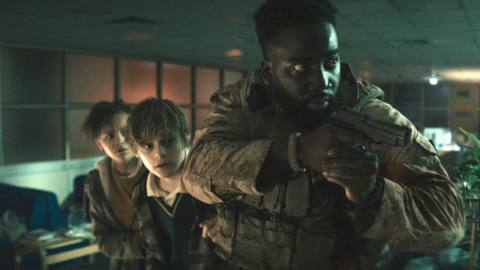 Trevante (Shamier Anderson) protects two young kids with his gun in Invasion
