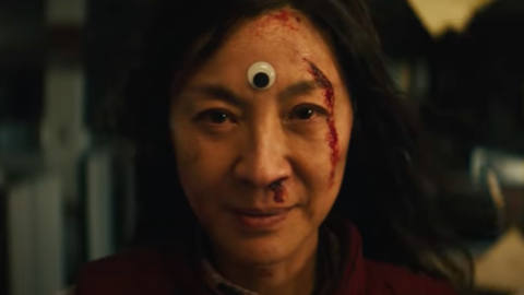 michelle yeoh staring at the camera, with a single googly eye on her forehead. she looks determined