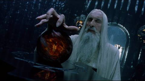 Saruman gestures with his hand claw-like over the Palantir — which shows the eye of Sauron wreathed in dark smoke — in The Lord of the Rings: The Fellowship of the Ring.