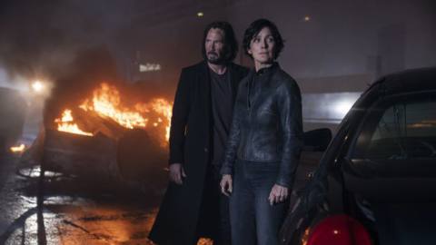 Neo and Trinity stand in front of burning wreckage in The Matrix Resurrections.