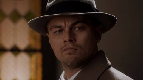 Leonardo DiCaprio in Shutter Island wearing his hat and standing in front of a lit window