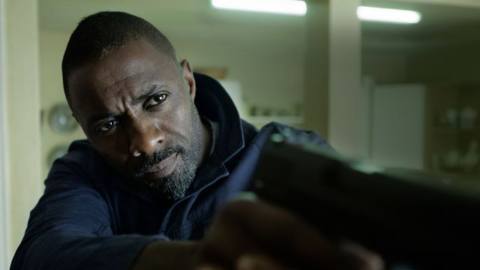 Idris Elba in The Take holding a gun at camera like he’s James Bond