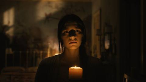 A still of a woman holding a candle illuminating her face in season 3 premiere of Servant