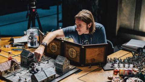 Matt Mercer sits behind his Critical Role DM divider and sets up a miniature on the map
