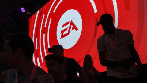 The silhouettes of attendees are seen standing in front of an Electronic Arts Inc. (EA) logo