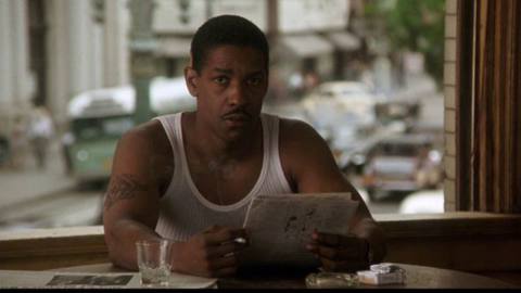 Denzel Washington, wearing a white tanktop, reads the newspaper in Devil in a Blue Dress.