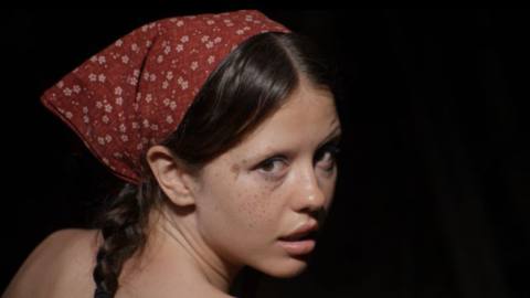 Mia Goth, shoulders bare and head in a kerchief, gives a come-hither look back over her shoulder in Ti West’s X