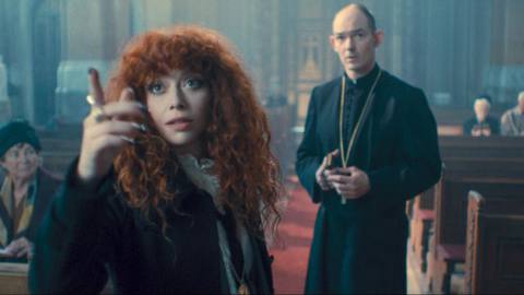nadia in russian doll. she is in a church, with a pastor behind her, pointing upwards