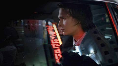 Ansel Elgort as Jake Adelstein in a car, with Tokyo lights reflected in the window in the HBO Max series Tokyo Vice.