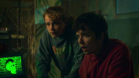 Asa Butterfield as Issac and Iola Evans as Kayla stare at a vivid green skull on an old CRT screen in Choose or Die