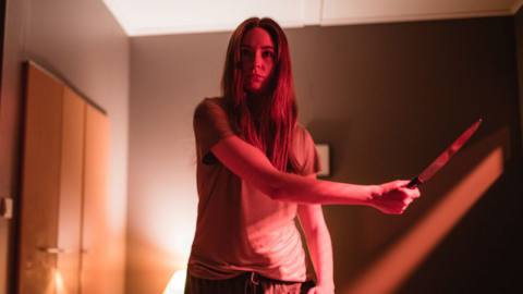 Karen Gillan stands under a red light, knife in hand, to practice her clone-murdering skills in Riley Stearns’ Dual