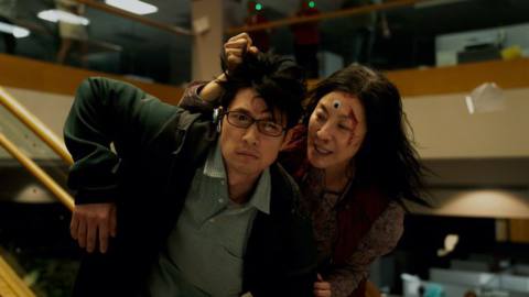 Michelle Yeoh, bloody and wearing a googly eye on her forehead, grabs Glee’s Harry Shum, Jr. by the hair during a fight scene in Everything Everywhere All At Once
