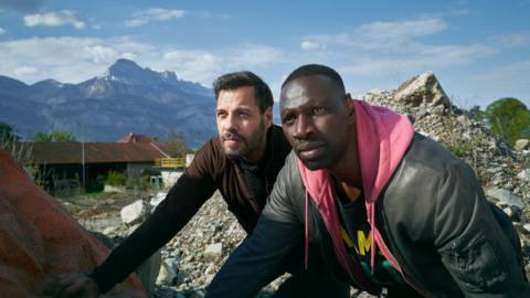 Laurent Lafitte and Omar Sy crouch behind a pile of rock and rubble in The Takedown