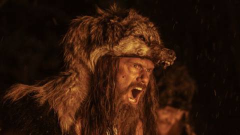 Alexander Skarsgard, wearing a wolf skin, howls during a firelight war ritual in The Northman