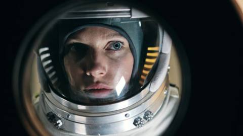 Hannah Wagner, dressed in a space suit, looks out of a porthole in Rubikon