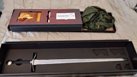 A box of Elden Ring goodies — including a whole-ass sword — sits on a bed