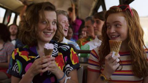 Eleven and Max smiling at each other on the bus with ice cream